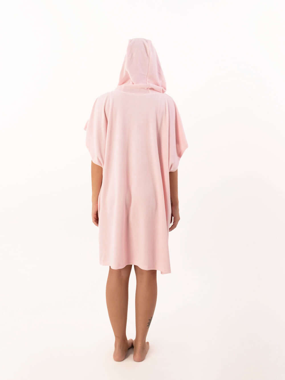 Modelo de poncho curto atoalhado rosa claro com capuz visto de costas.