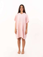 Modelo usando poncho curto atoalhado rosa claro com bolso canguru, ideal para praia e esportes aquáticos.