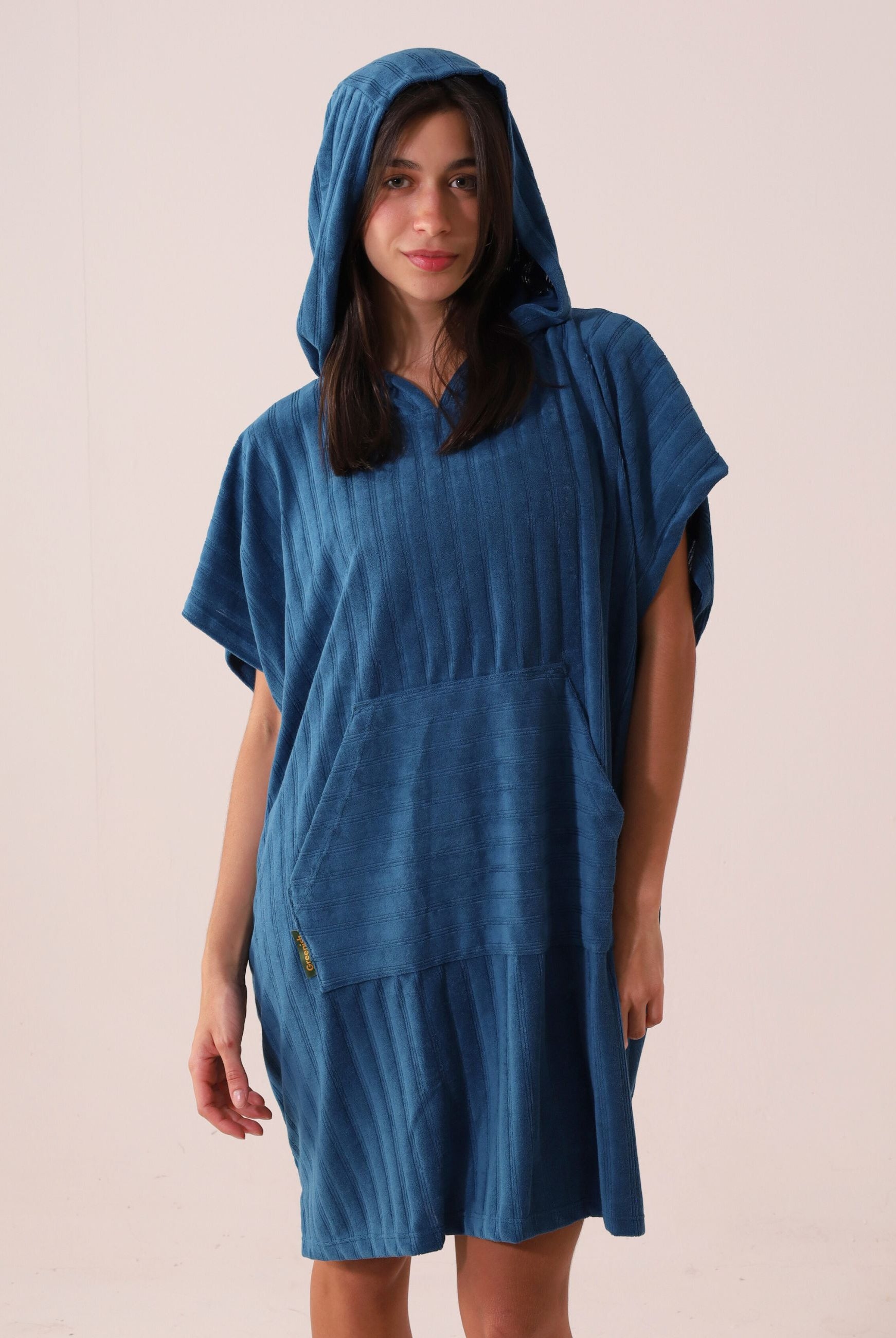 Mulher vestindo PONCHO CURTO CANELADO - AZUL da marca Greenish, ideal para aquecer e trocar na praia, com bolsos frontais e tecido atoalhado.