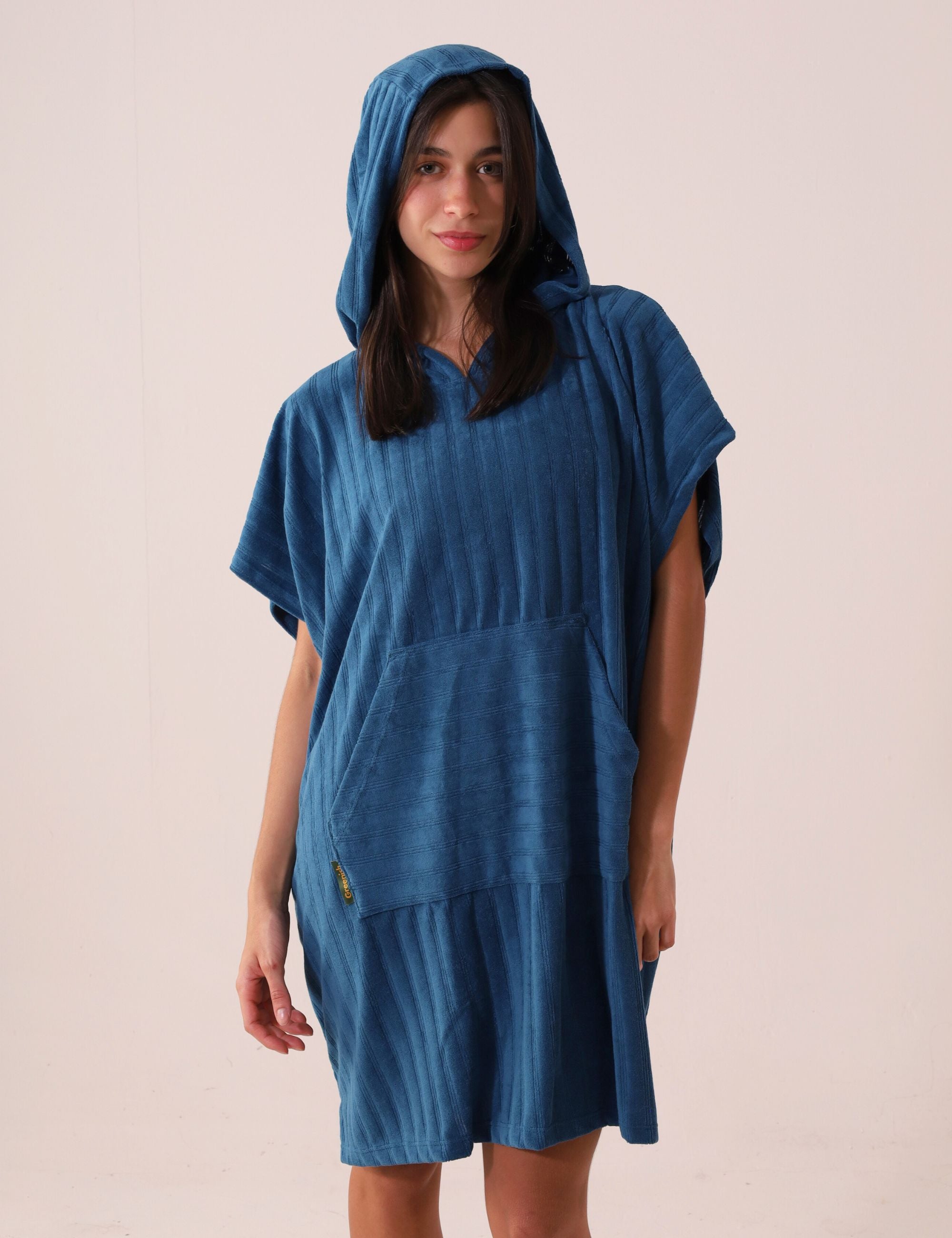 Mulher vestindo PONCHO CURTO CANELADO - AZUL da marca Greenish, ideal para aquecer e trocar na praia, com bolsos frontais e tecido atoalhado.