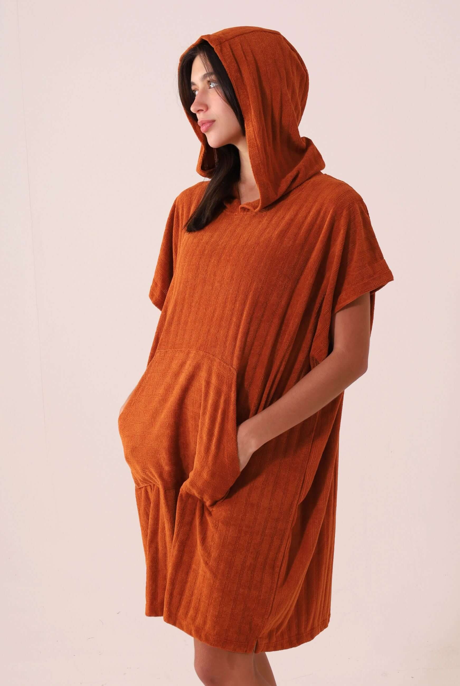 Mulher vestindo PONCHO CURTO CANELADO - CARAMELO da marca Greenish, com bolsos canguru, capuz, tecido atoalhado e secagem rápida.