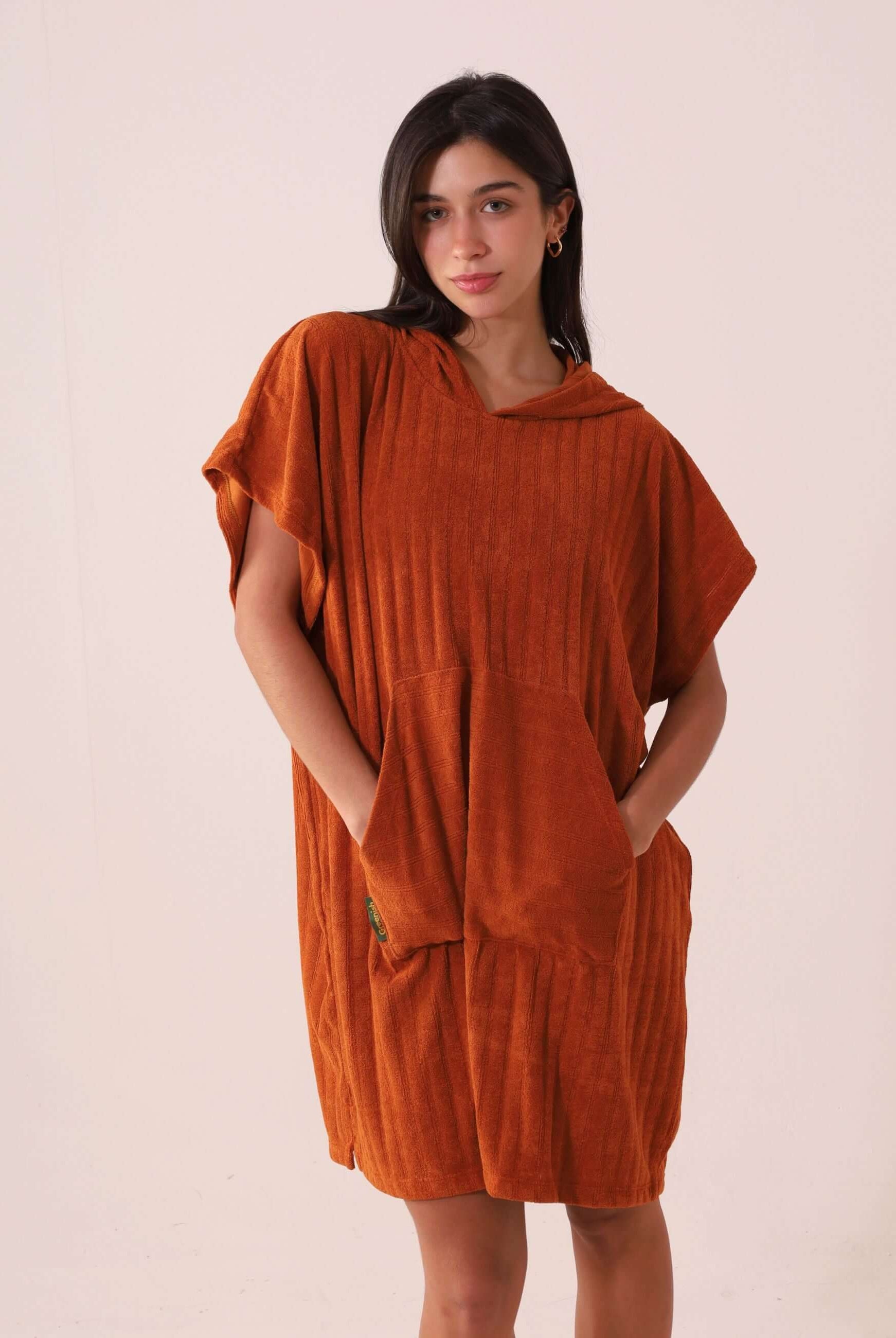 Mulher vestindo PONCHO CURTO CANELADO - CARAMELO da Greenish, destacando design casual e prático, ideal para praia e esportes aquáticos.