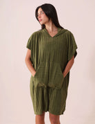 Mulher vestindo PONCHO CURTO CANELADO - VERDE da Greenish, com bolsos modelo canguru e tecido atoalhado, ideal para esportes aquáticos.