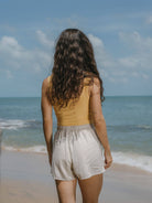 Mulher de costas na praia usando regata Kora amarelo da Greenish, refletindo estilo e conforto.