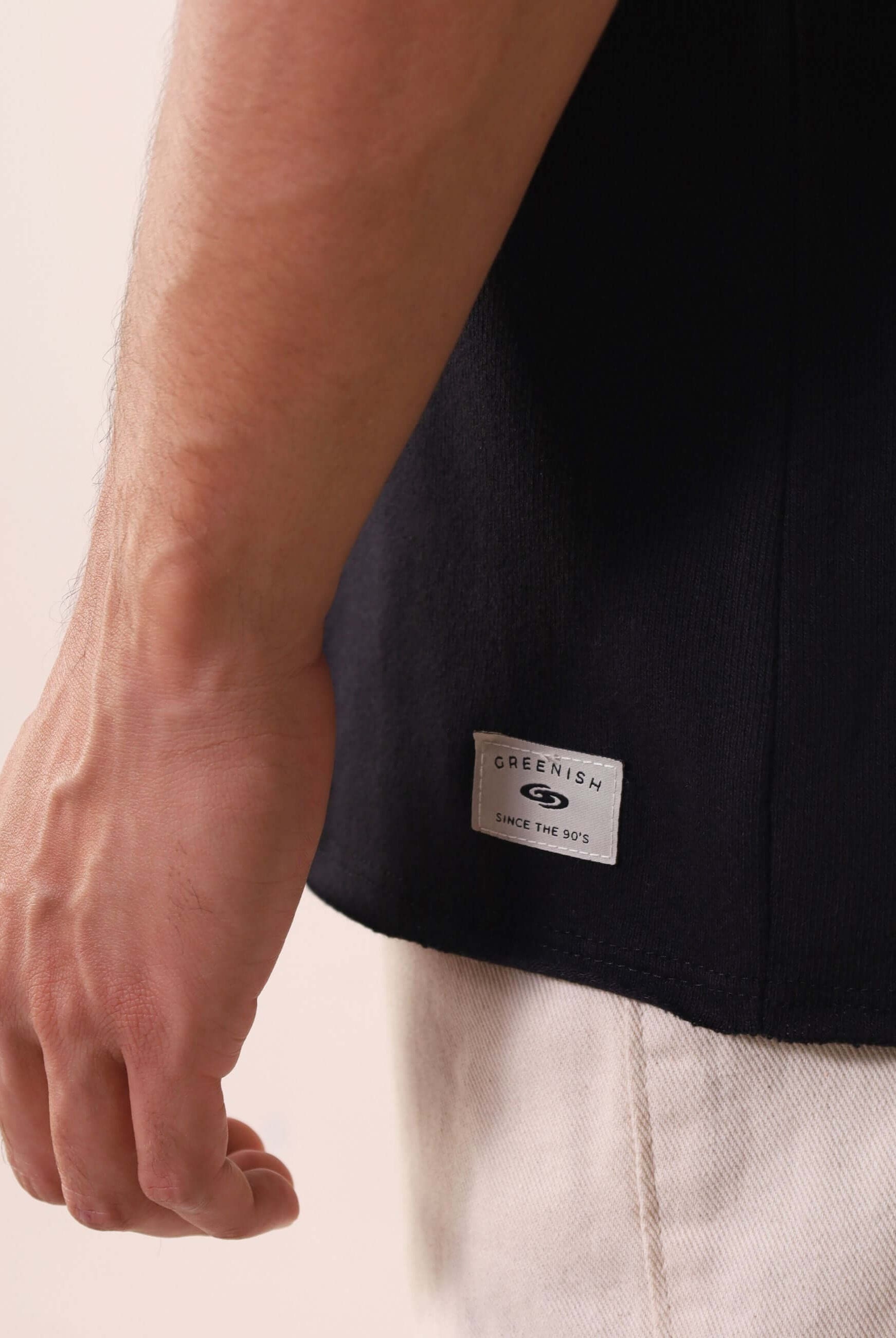 Detalhe da REGATA LARGA WAVES - PRETO da Greenish com etiqueta na base, tecido 100% algodão para conforto diário ao ar livre.