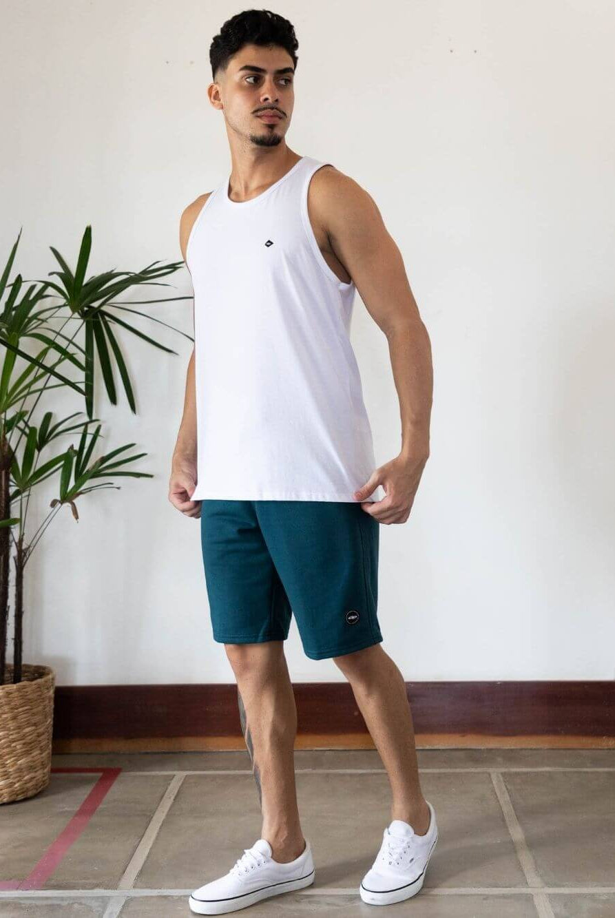 Model wearing Regata Malha Basic branca da Greenish, com calção e tênis brancos, em ambiente moderno.