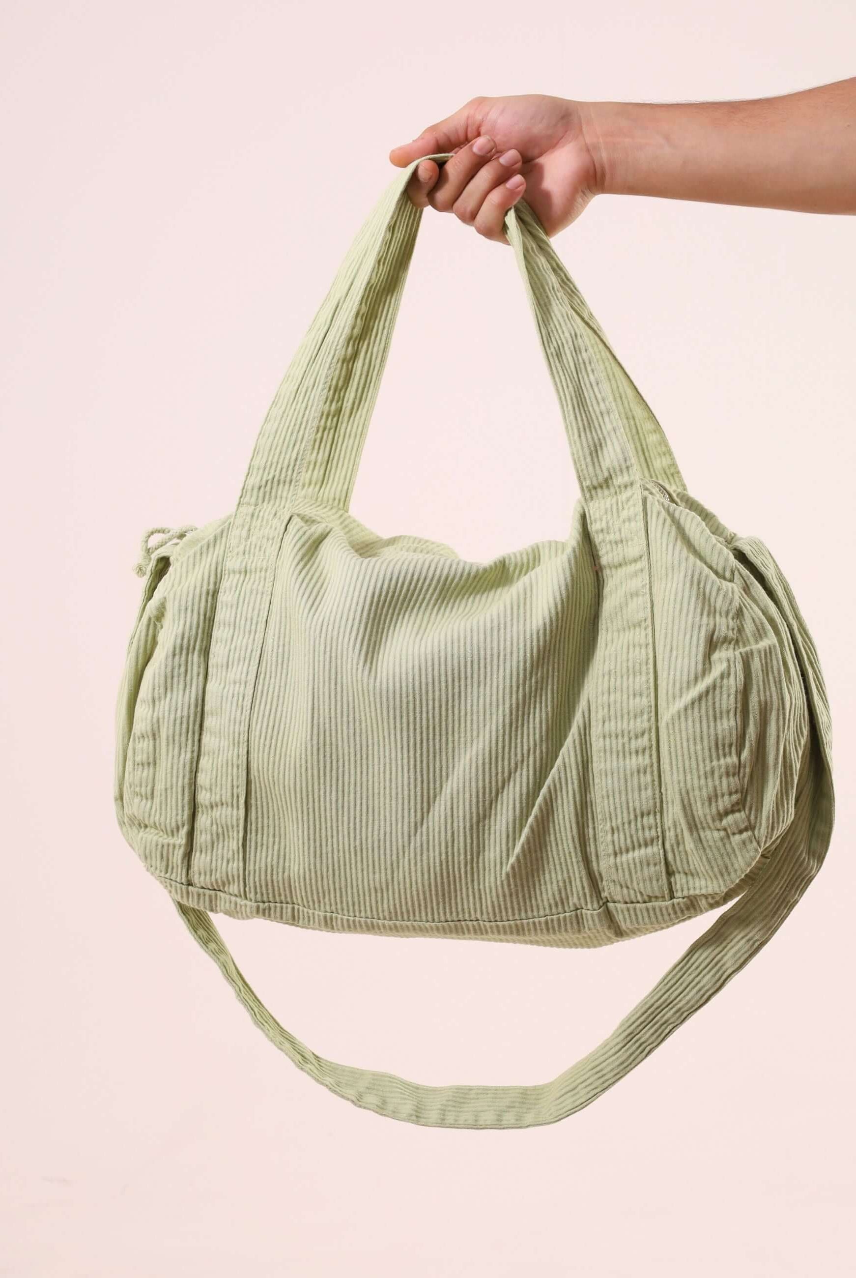 Pessoa segurando Sacola Duffel Bag - Verde Claro, feita de sarja peletizada e alças reforçadas, ideal para uso diário e estilo ao ar livre.