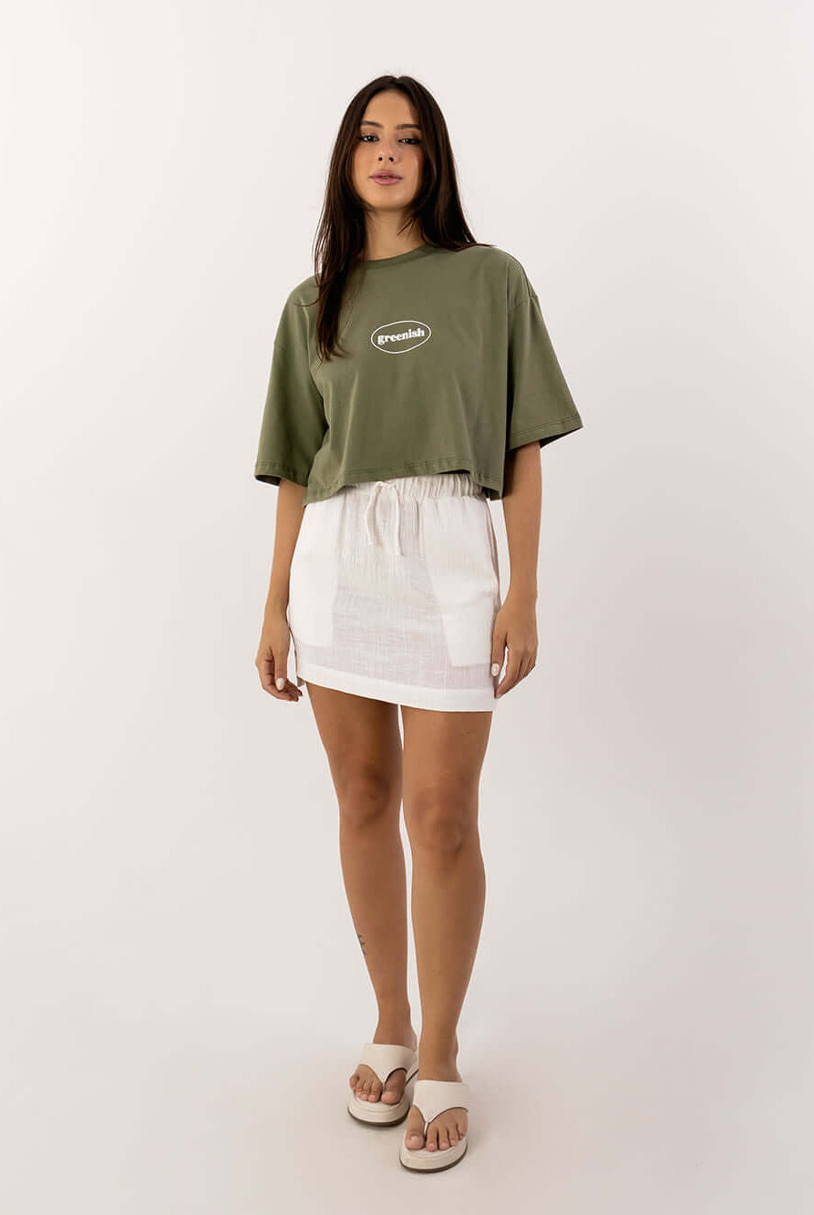 Modelo usando saia curta Íris off white da Greenish, com camiseta verde e sandálias, estilo casual e trendy.