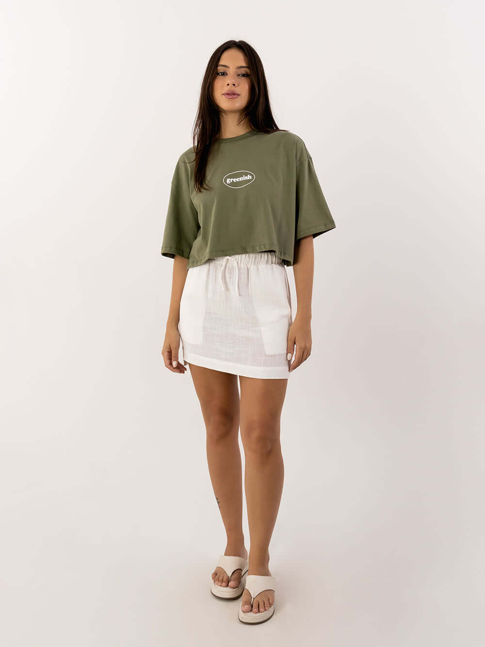 Modelo usando saia curta Íris off white da Greenish, com camiseta verde e sandálias, estilo casual e trendy.