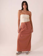 Mulher vestindo SAIA MIDI DÉA - CHOCOLATE da Greenish; saia reta e canelada, cós elástico com cadarço, fenda lateral direita.
