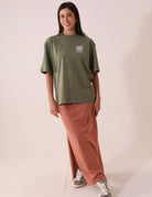 Mulher vestindo SAIA MIDI DÉA - CHOCOLATE da Greenish com camiseta verde, mostrando estilo e conforto com fenda lateral direita.