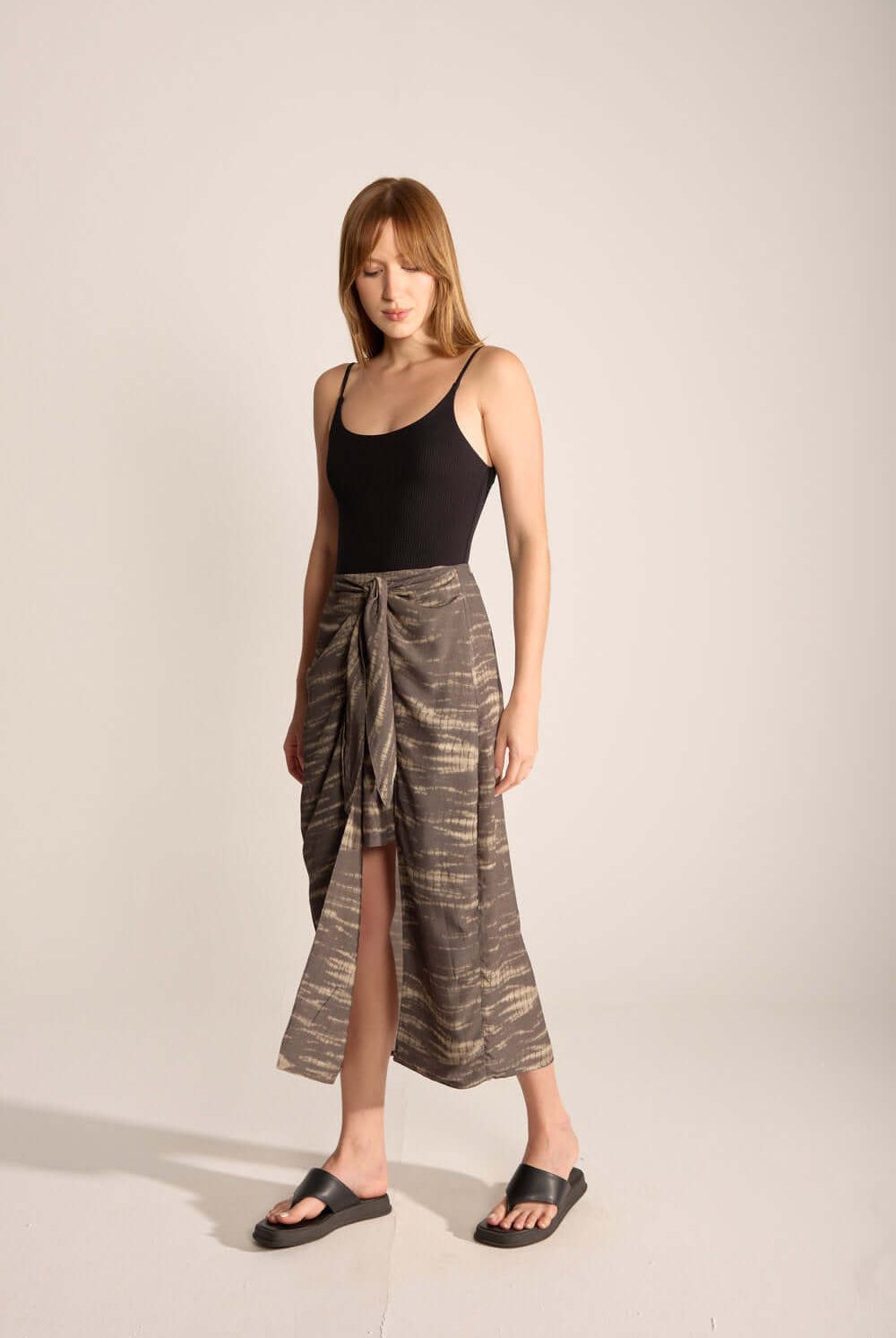 Woman in a black swimsuit wearing a chic tie dye midi skirt, showcasing a relaxed outdoor style.