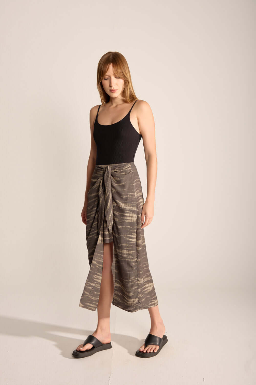 Woman in a black swimsuit wearing a chic tie dye midi skirt, showcasing a relaxed outdoor style.