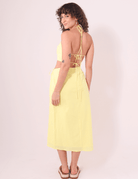 Mulher com Saia Midi Sunny Amarelo Greenish, de costas, exibindo design leve e confortável ideal para dias ensolarados.
