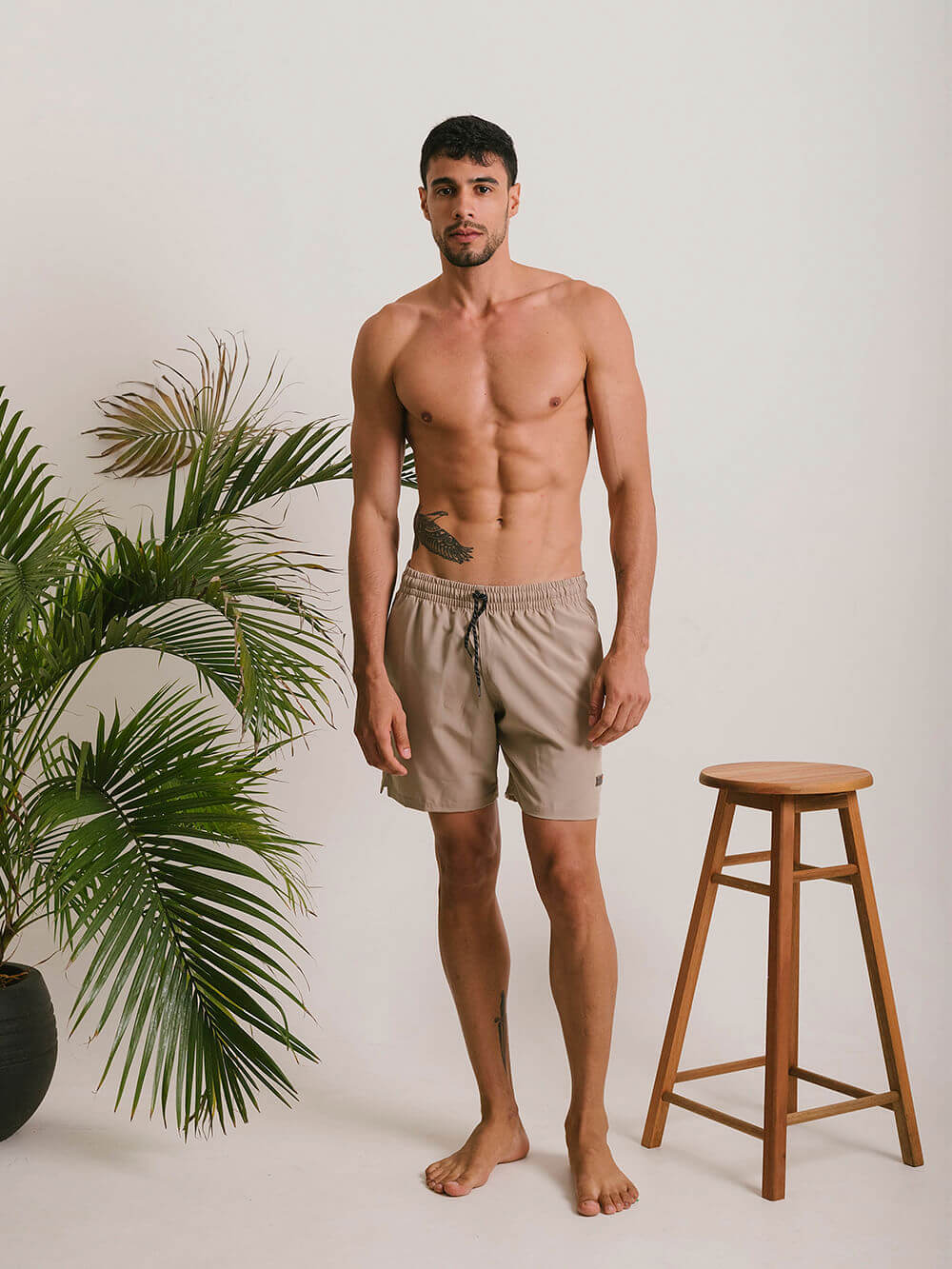 Short Fitness Basic bege da Greenish, modelo masculino em ambiente descontraído com plantas.