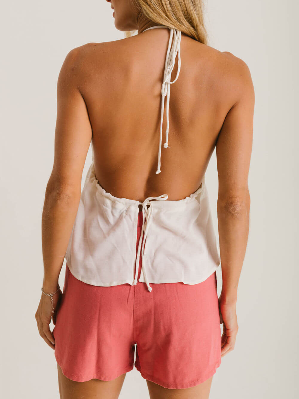 Vista traseira de blusa com amarração da Greenish, combinada com shorts rosa, mostrando caimento elegante.