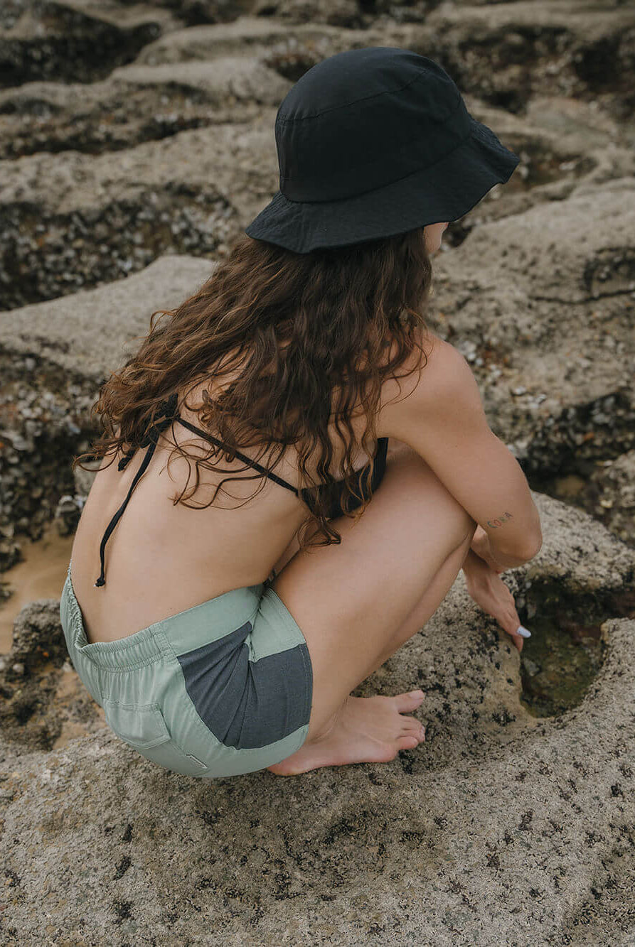 Modelo usando Short Sport Sidecut Verde da Greenish, explorando rochas na praia com estilo e conforto.