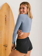 Mulher sorridente usando short sport Preto da Greenish, perfeito para surfe e atividades ao ar livre em dia de praia.