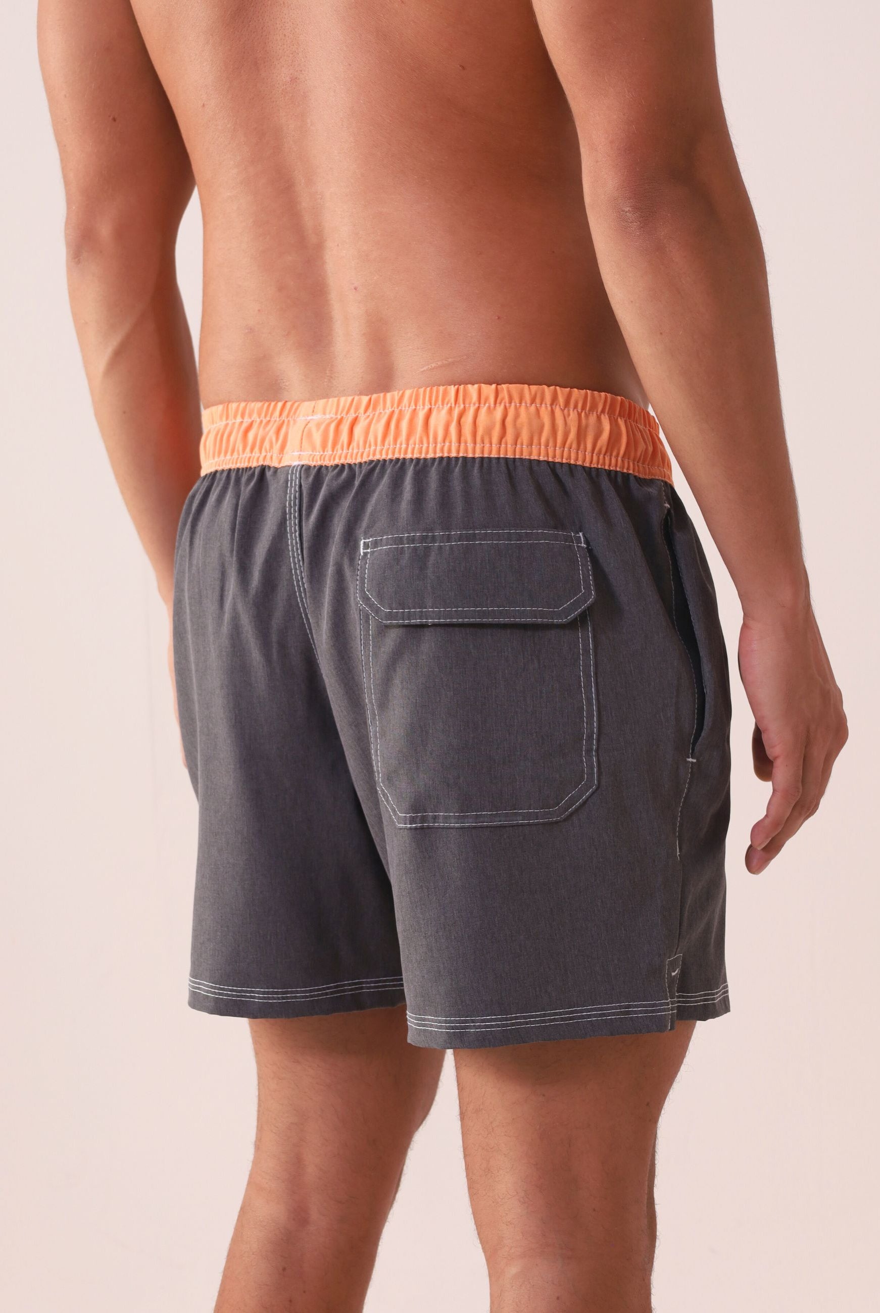 Modelo usando Short Vôley Blend - Grafite da Greenish com cós laranja, bolso traseiro e costura branca contrastante.