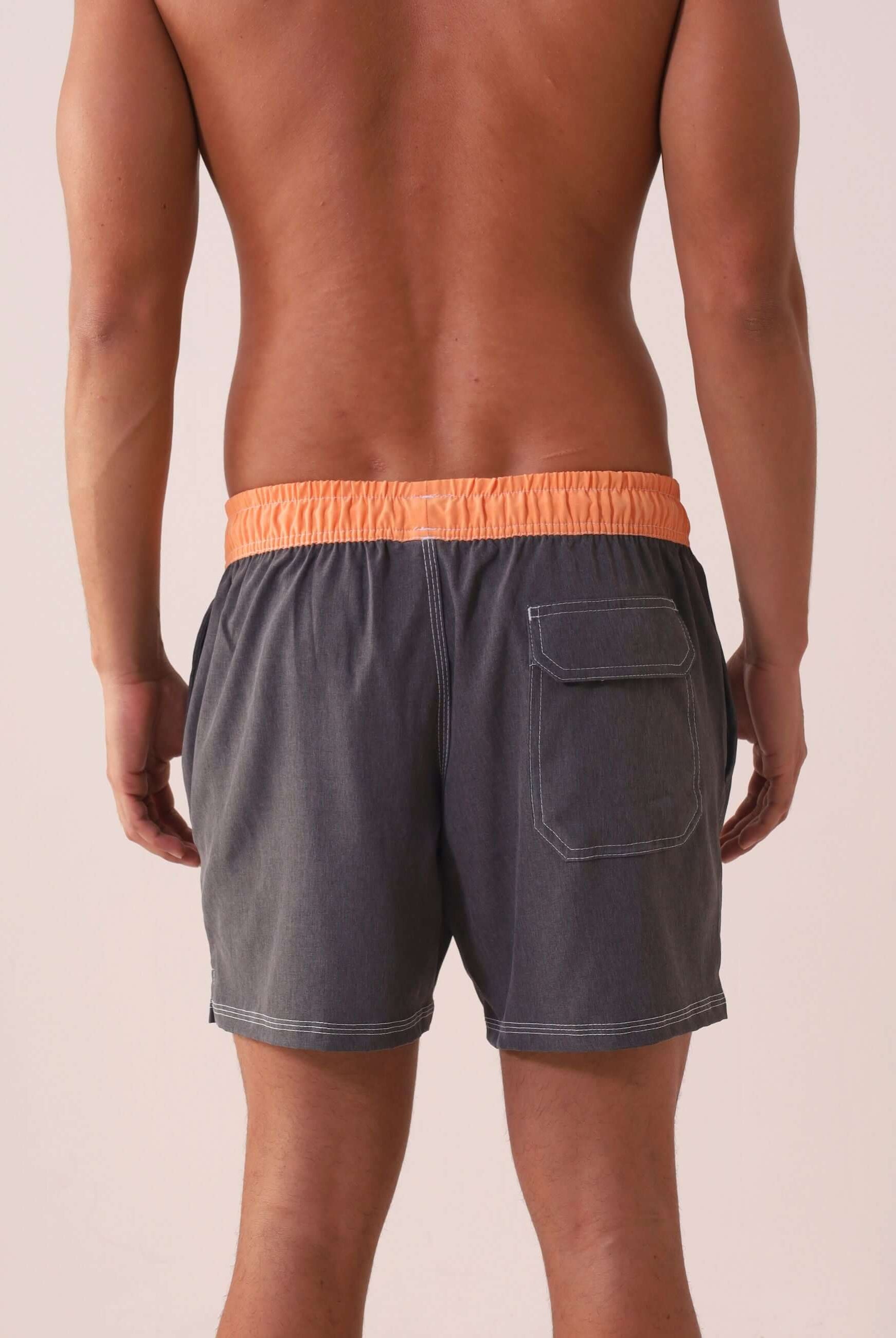 Homem usando SHORT VÔLEY BLEND - GRAFITE da Greenish com cós laranja, bolso traseiro e costura branca em contraste.