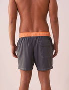 Homem usando SHORT VÔLEY BLEND - GRAFITE da Greenish com cós laranja, bolso traseiro e costura branca em contraste.