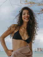 Sutiã Bíquini Hike Preto da Greenish em modelo cortininha, mulher sorridente na praia, look verão.