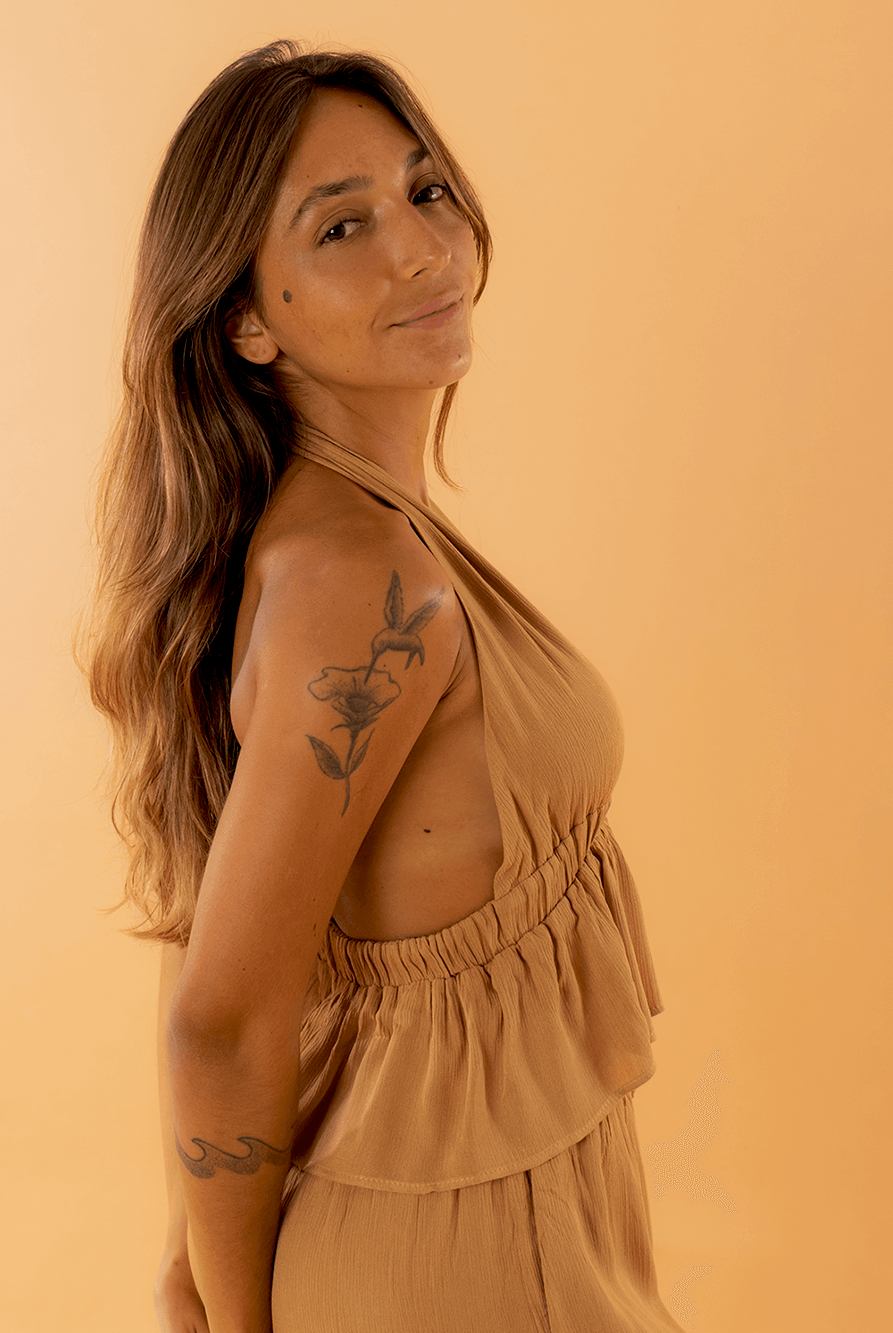 Modelo usando o top Eliza na cor caqui da marca Greenish, em fundo laranja.