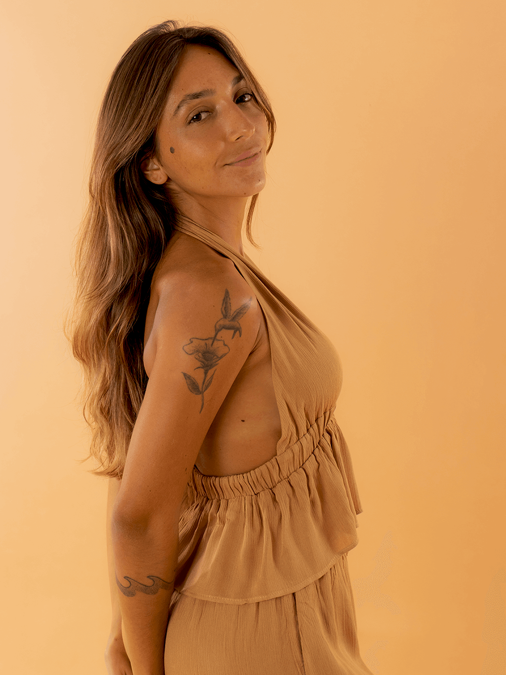 Modelo usando o top Eliza na cor caqui da marca Greenish, em fundo laranja.