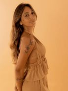 Modelo usando o top Eliza na cor caqui da marca Greenish, em fundo laranja.