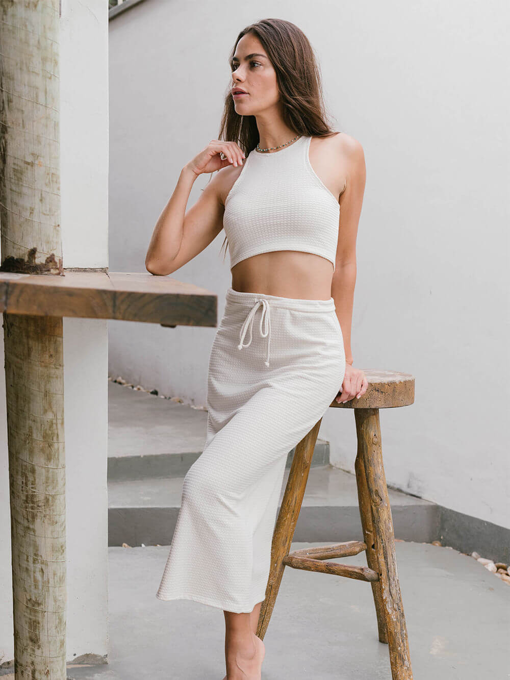 Modelo usando top tricot Issy bege da Greenish, cropped ajustado e versátil, em ambiente moderno e ao ar livre.