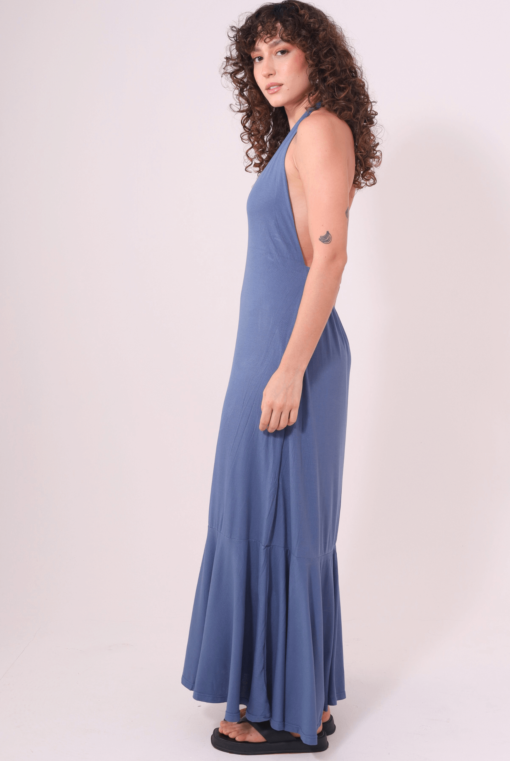 Alt Tag: Mulher vestindo Vestido Longo Serea Azul Jeans da Greenish, com decote profundo e detalhe jabô na barra para um look leve e marcante.