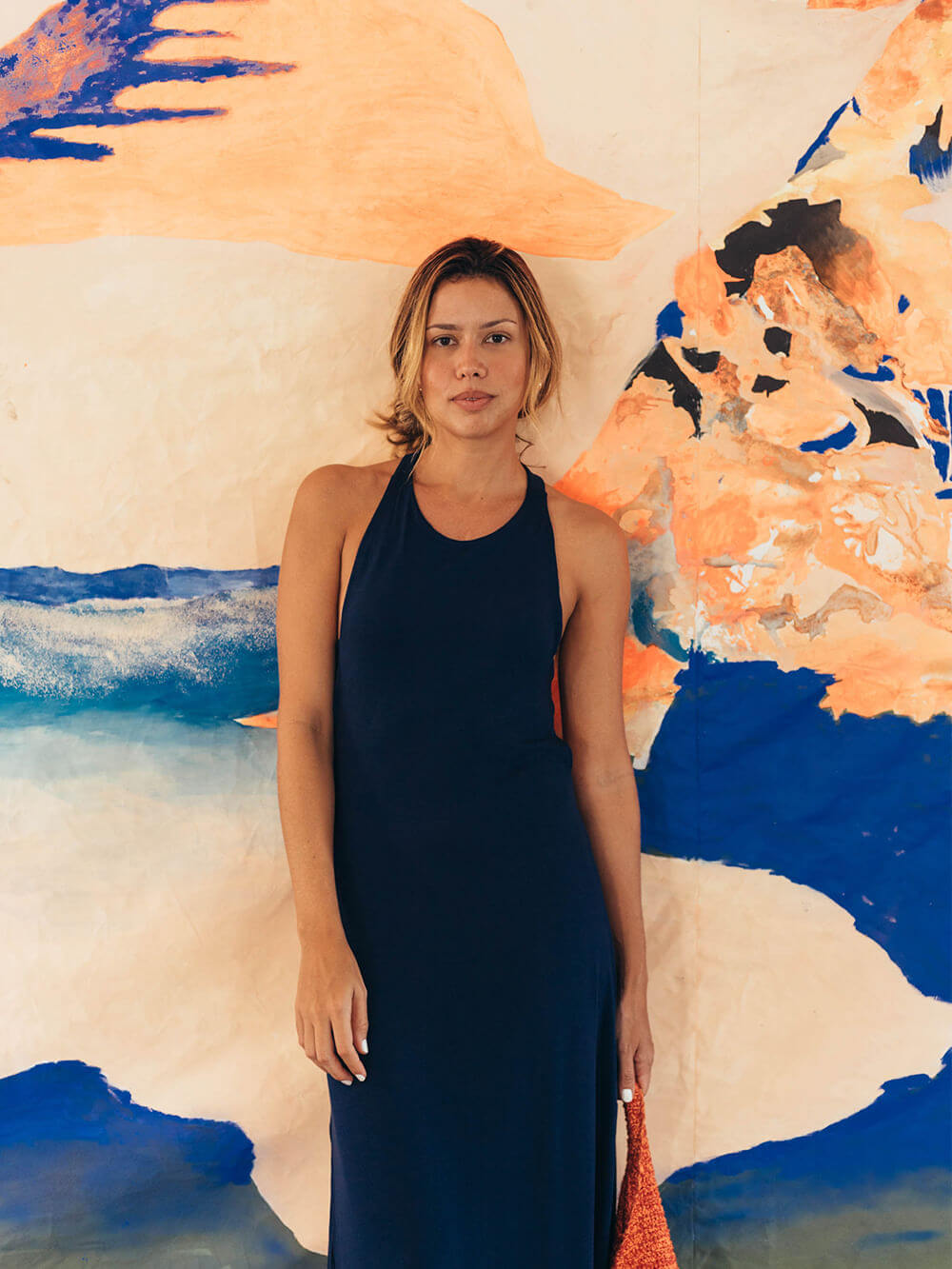 Mulher usando vestido midi azul marinho Frankie da marca Greenish, em fundo artístico colorido.