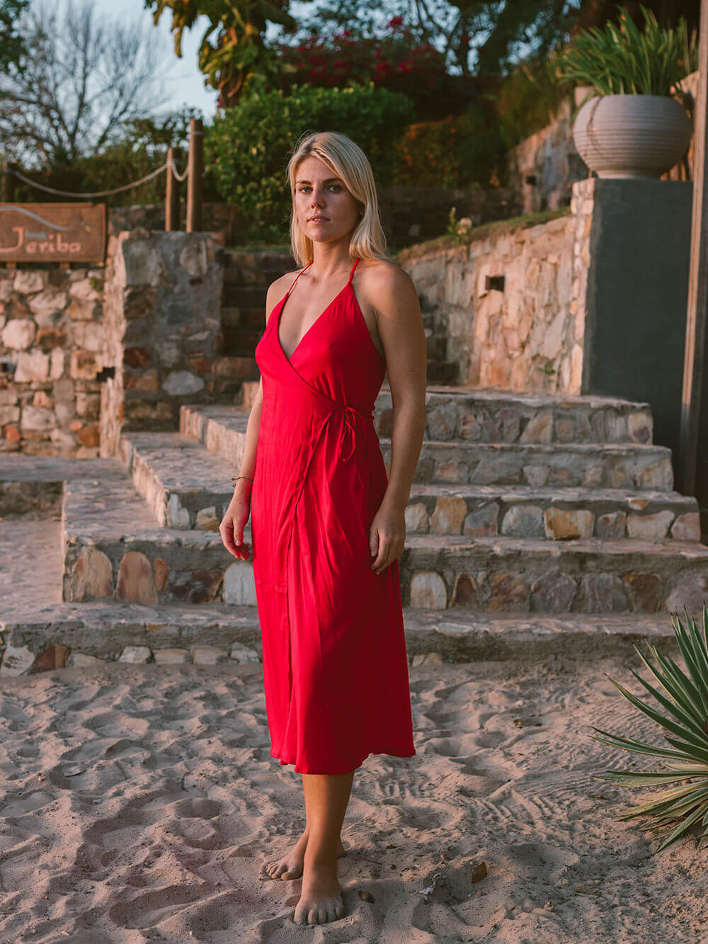 Modelo vestindo vestido midi redondo bordô da Greenish, em ambiente ao ar livre com pedras e plantas.