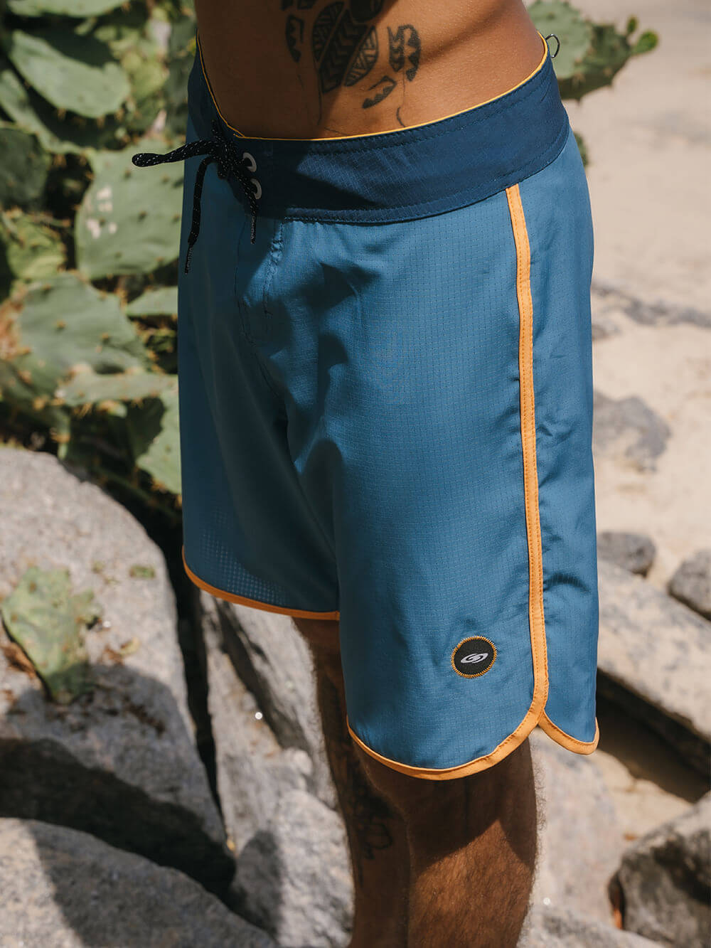 Bermuda de praia Retrô Flat Sea da Greenish em azul, com detalhes laranja e cordão de ajuste.