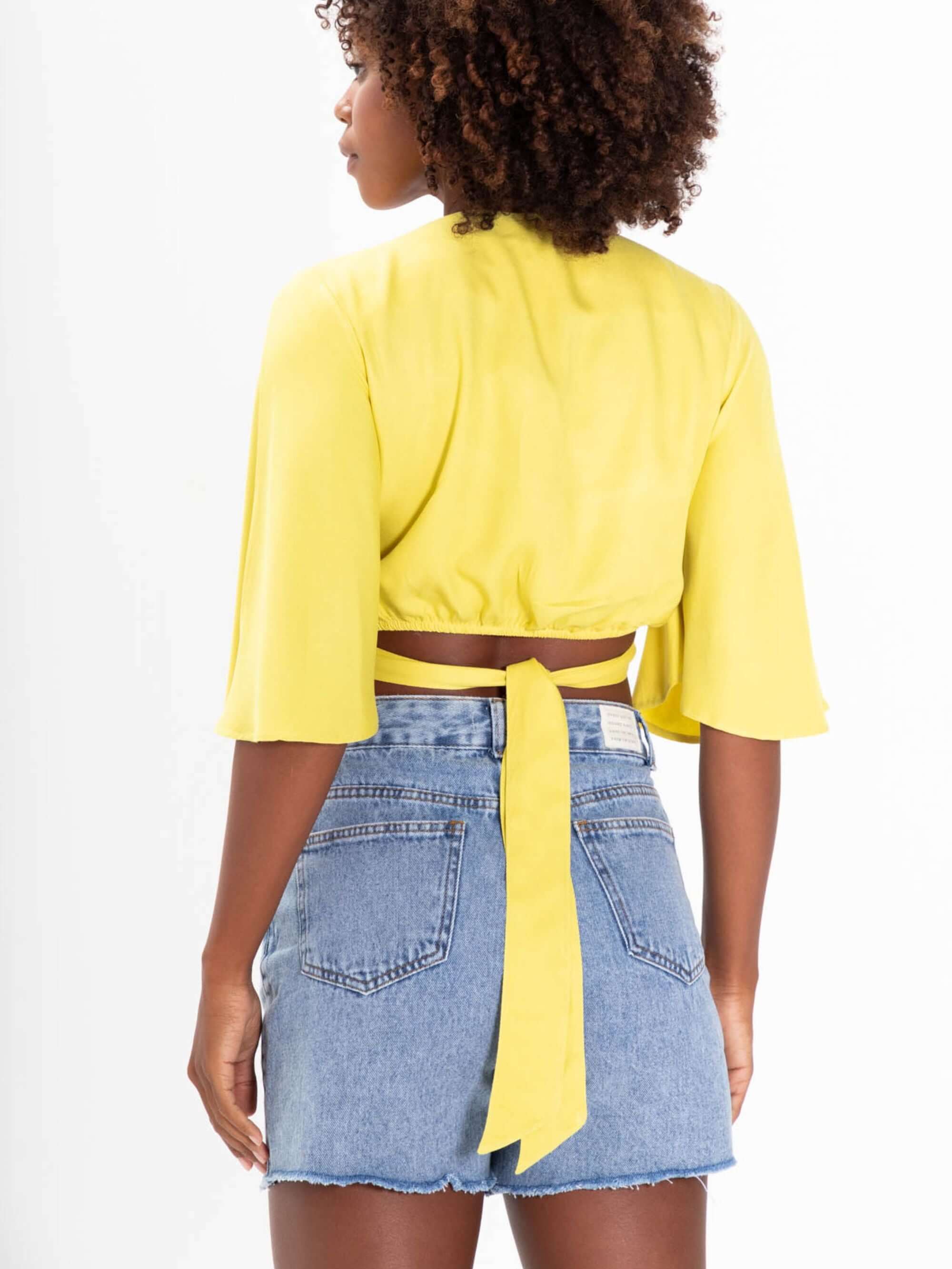 Cropped Lani da Greenish, em amarelo, com mangas soltinhas e amarração nas costas para ajuste confortável.