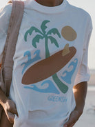 Camiseta oversized off white da Greenish com estampa tropical de surfe e palmeiras, ideal para o vibe da praia.