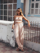 Mulher vestindo blusa cropped Cecilia bege da Greenish, usando óculos de sol e calças largas, em ambiente urbano.