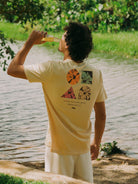 Camiseta Hibiscus amarela da Greenish, com estampa colorida, vista por homem em natureza, segurando bebida refrescante.