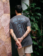 Alt Tag: Homem vestindo camiseta Grafite 'The Seed, The Sun and Moon' da Greenish com estampa de equilíbrio natural em um jardim.