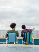 Dois homens relaxando em cadeiras de praia, observando o horizonte em um dia nublado.