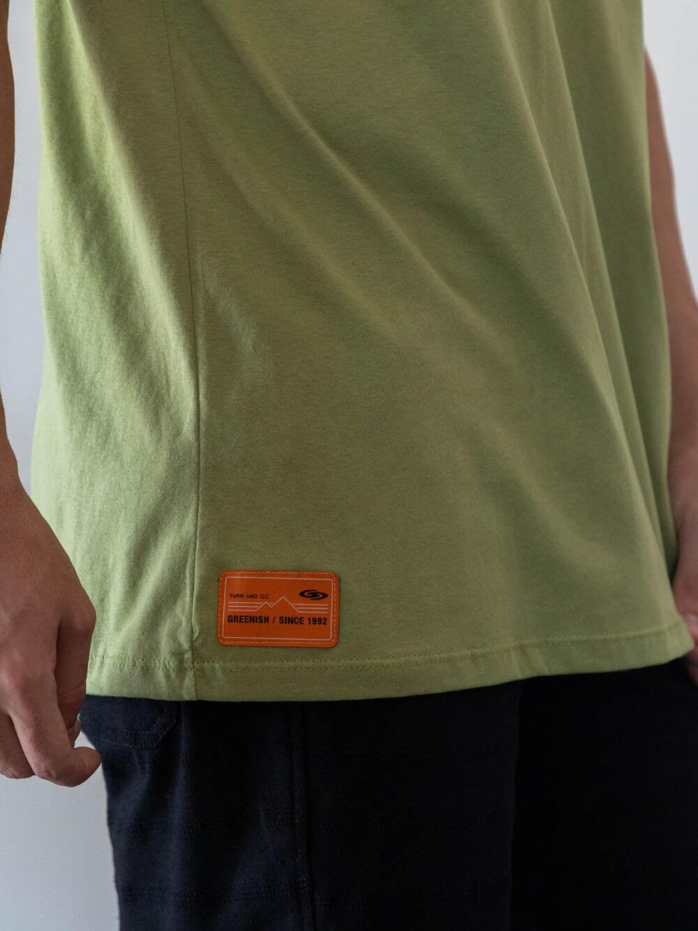 Camiseta oversized verde da marca Greenish, destacando o detalhe da etiqueta na lateral.