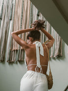 Top cropped branco da Greenish, mostrando detalhes das costas e amarração, com fundo estiloso de cordas.