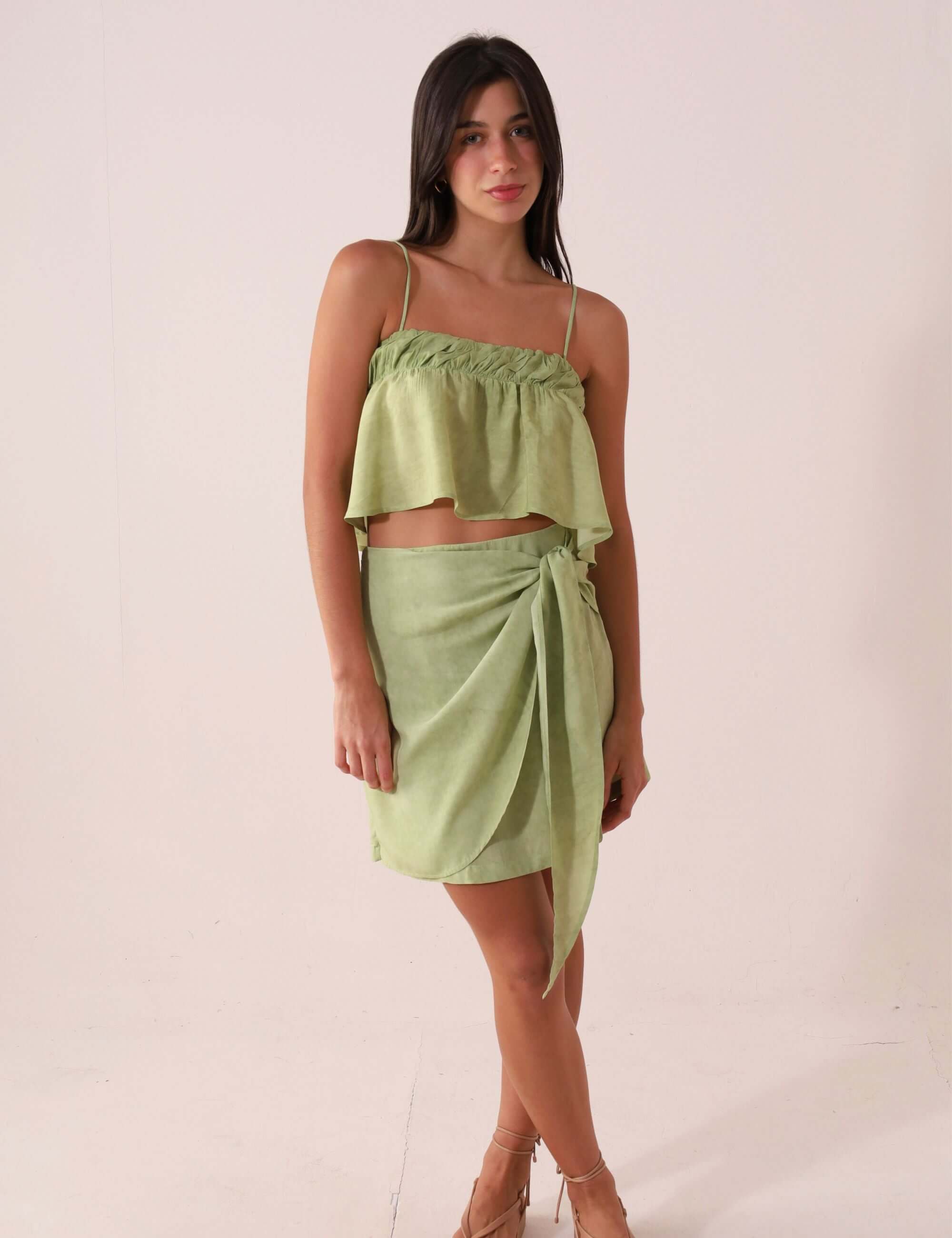 Mulher vestindo SAIA CURTA THÁ - VERDE da Greenish, feita de viscose com cintura alta e amarração lateral, destacando visual elegante.