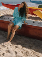 Modelo vestindo macaquinho Suzy turquesa da Greenish na praia, sentada em barco colorido, look prático e fluido.