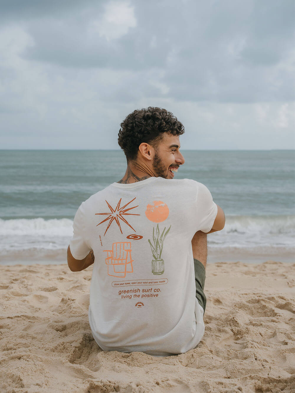 Camiseta Greenish Natural Elements na praia, destacando estampa de natureza e relaxamento.
