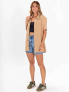 Modelo usando blusa Agatha Bege da Greenish, combinada com shorts jeans e tênis, estilo casual e moderno.