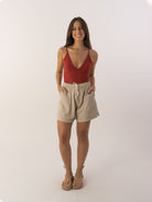 Modelo usando o Top Liz da marca Greenish, com shorts claros, sorriso alegre em fundo neutro.