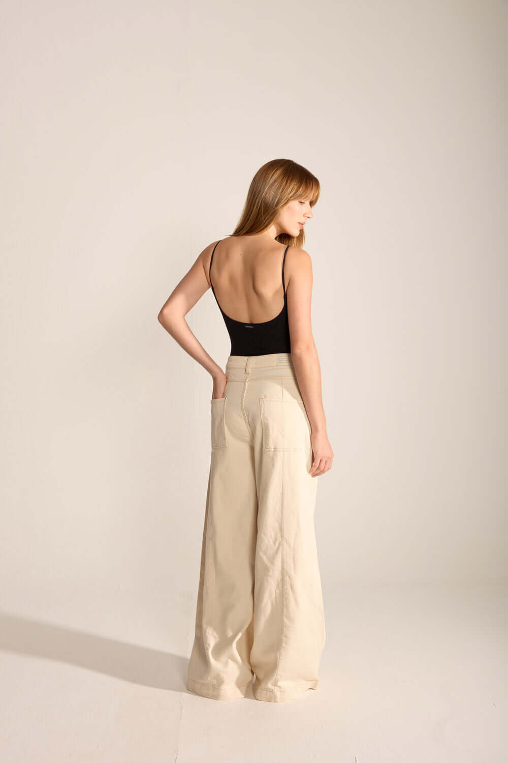 Modelo usando body preto feminino da marca Greenish, vista de costas, com calça larga em tom claro.