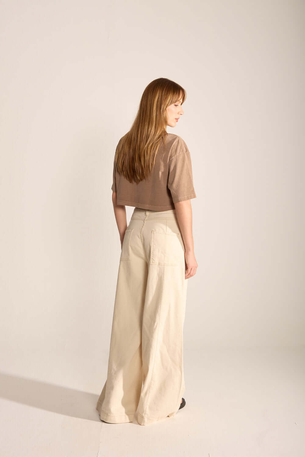 Modelo usando a Calça Laila da Greenish, estilo wide leg, em fundo neutro, mostrando recortes e conforto contemporâneo.