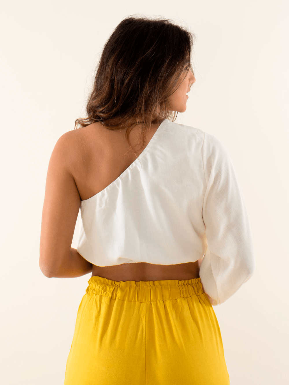 Blusa Tati off white da Greenish, estilo assimétrico, visto de costas com calça amarela.